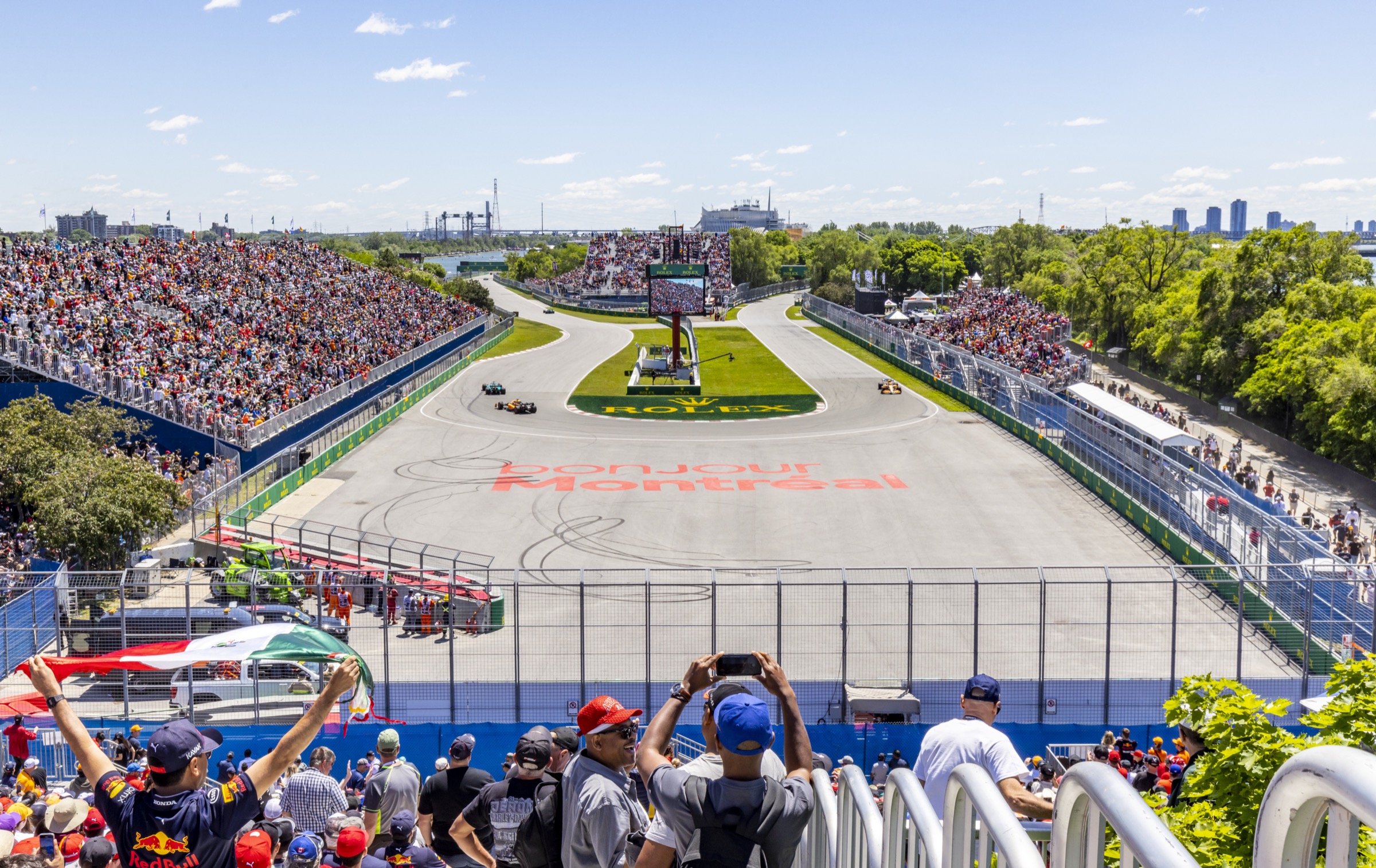 Wide F1 weekend track shot at Circuit Gilles-Villeneuve, packed grandstand and infield, Montreal skyline in background